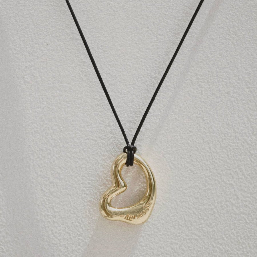 18-carat gold plated abstract heart motif pendant on a black leather cord, showcasing the Fluidic Amore necklace’s modern design | ANI EGOISTA